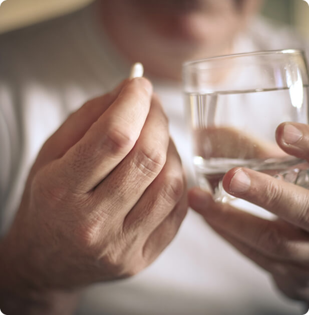 prikazani sta dve moški roki. v eni roki drži tableto proti bolečinam, v drugi pa kozarec vode